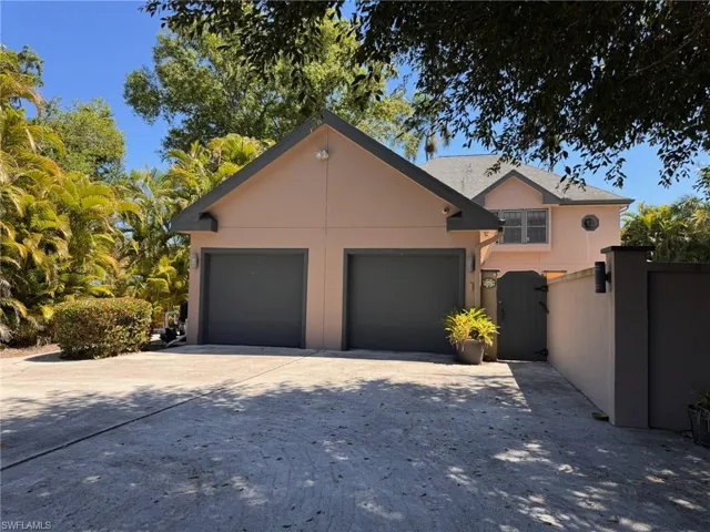 View of back of house with a gate, fence, an attached garage, stucco siding, and driveway