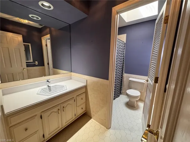 2nd bathroom featuring tile patterned floors, toilet, vanity, wainscoting, and tile walls
