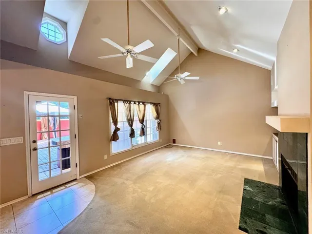 Living room featuring ceiling fan, a tiled fireplace, a high ceiling, and light carpet