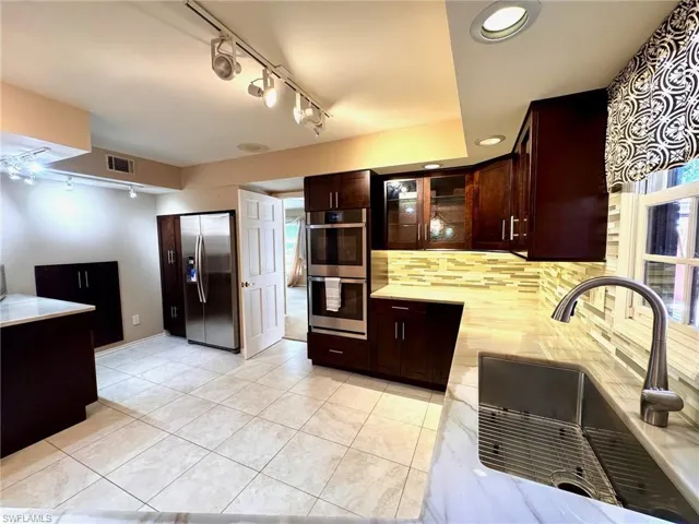 Kitchen with stainless steel appliances, light countertops, backsplash, dark brown cabinetry, and glass insert cabinets