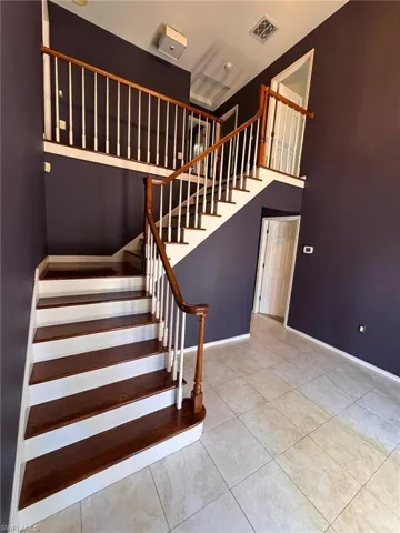 Staircase featuring a high ceiling, tile patterned flooring, and wooden stair treads and banisters