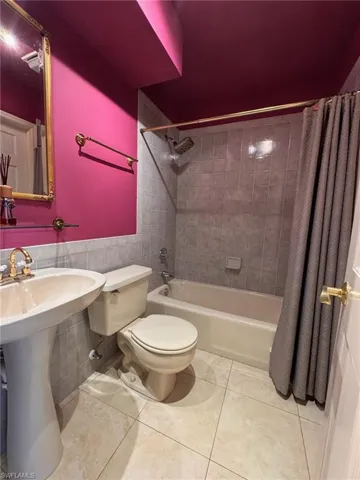 1st floor bathroom featuring tile walls, toilet, shower / bath combo with shower curtain, tile patterned flooring, and wainscoting