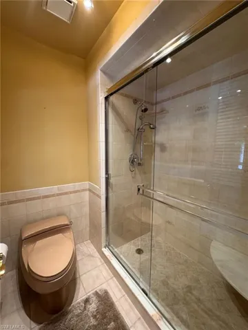 Primary bathroom with tile walls, toilet, a wainscoted wall, tile patterned floors, and a stall shower