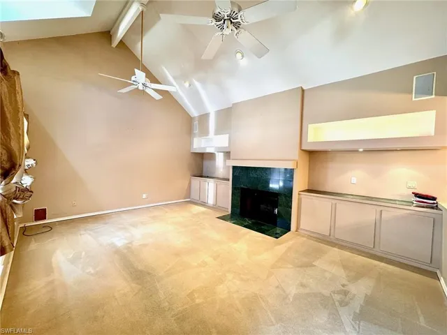 Unfurnished living room featuring a ceiling fan, beam ceiling, light carpet, a tiled fireplace, and high vaulted ceiling
