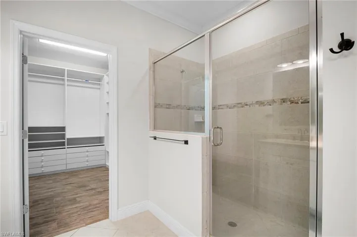 Bathroom featuring a stall shower, a walk in closet, light tile patterned floors, and crown molding