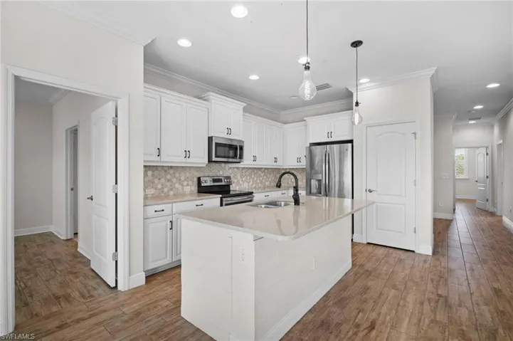 Kitchen with stainless steel appliances, white cabinetry, an island with sink, decorative light fixtures, and crown molding