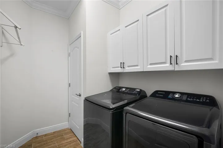 Laundry area featuring wood finish floors, crown molding, cabinet space, and washer and clothes dryer