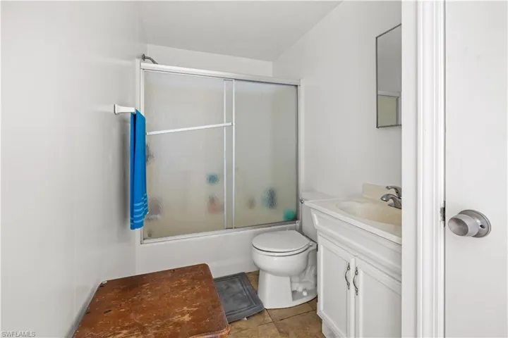Full bathroom with tile flooring, bath / shower combo with glass door, large vanity, and toilet in apartment