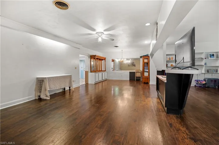 Living room featuring ceiling fan with notable chandelier and dark hardwood / wood-style flooring