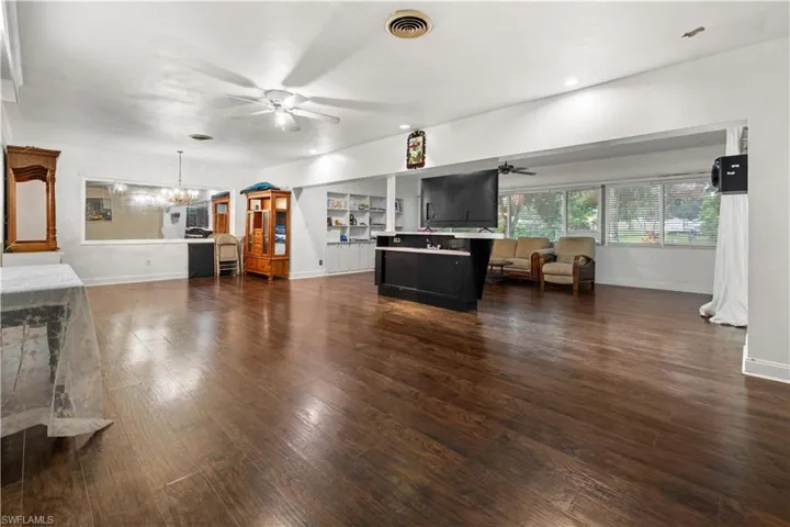 Living room with ceiling fan with notable chandelier and dark hardwood / wood-style flooring