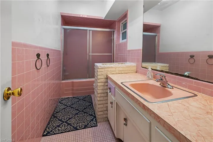 Bathroom with tile flooring, oversized vanity, enclosed tub / shower combo, and tile walls