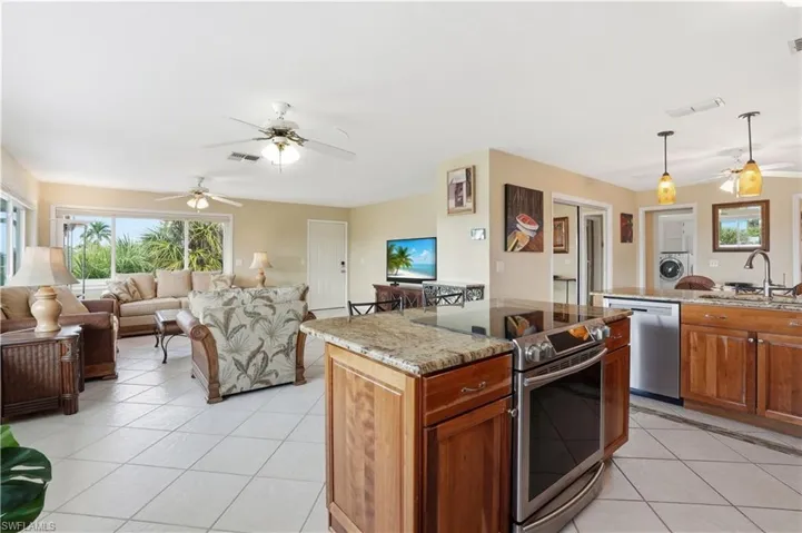 Kitchen featuring a ceiling fan, light stone counters, brown cabinetry, appliances with stainless steel finishes, and hanging light fixtures - Virtually Edited Image