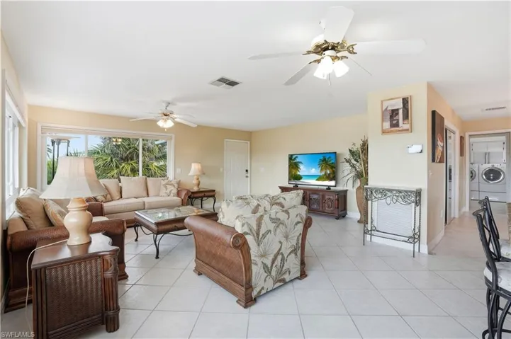 Living area with washer and dryer, light tile patterned floors, and ceiling fan - Virtually Edited Image