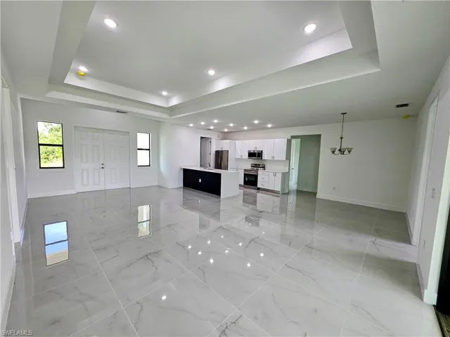 Unfurnished living room with light tile patterned flooring, a raised ceiling, and a chandelier