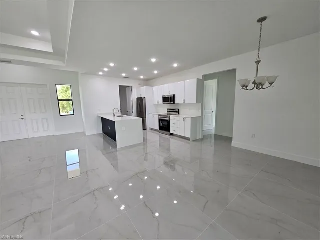 Kitchen with stainless steel appliances, white cabinets, light tile patterned floors, and decorative light fixtures