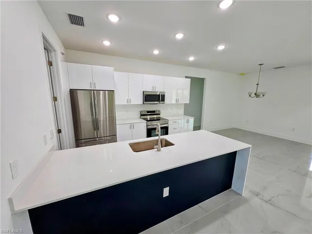 Kitchen featuring light tile patterned flooring, sink, decorative light fixtures, stainless steel appliances, and white cabinets
