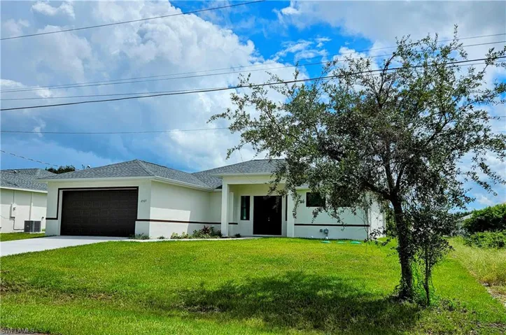 View of front of property featuring a garage, central AC unit, and a front yard