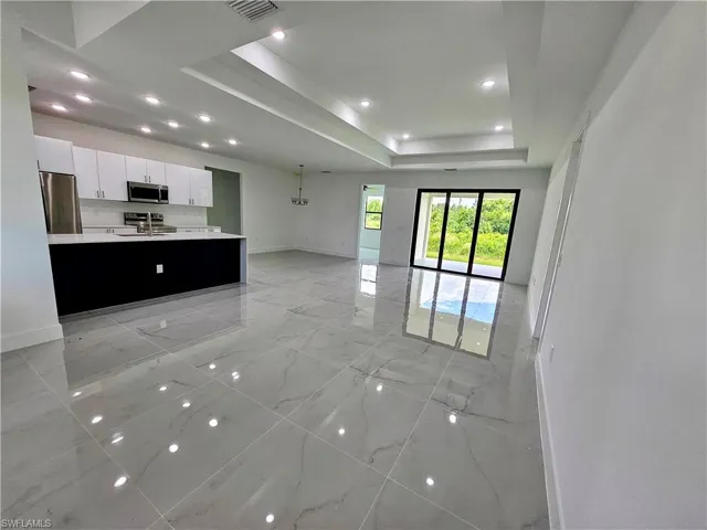 Kitchen with light tile patterned flooring, appliances with stainless steel finishes, a kitchen island with sink, a tray ceiling, and white cabinets