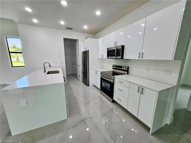Kitchen featuring sink, stainless steel appliances, light tile patterned flooring, and white cabinetry