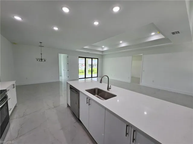 Kitchen with dishwasher, white cabinetry, sink, a tray ceiling, and hanging light fixtures
