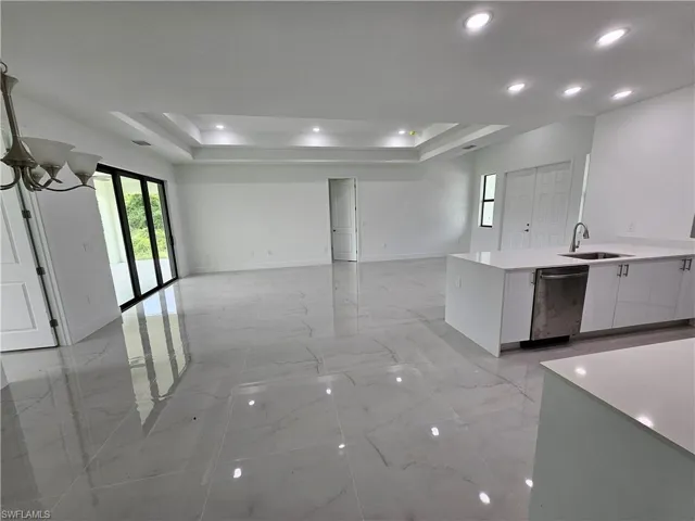 Kitchen featuring white cabinetry, stainless steel dishwasher, sink, a raised ceiling, and light tile patterned flooring