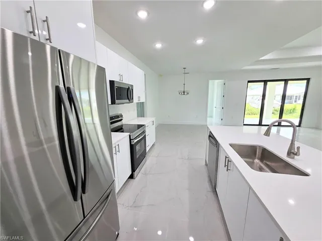 Kitchen with light tile patterned flooring, sink, appliances with stainless steel finishes, white cabinetry, and hanging light fixtures