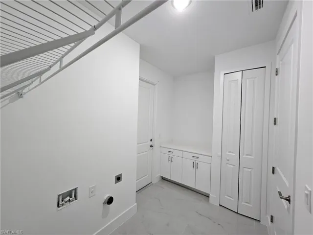 Laundry area with hookup for an electric dryer, light tile patterned flooring, and washer hookup