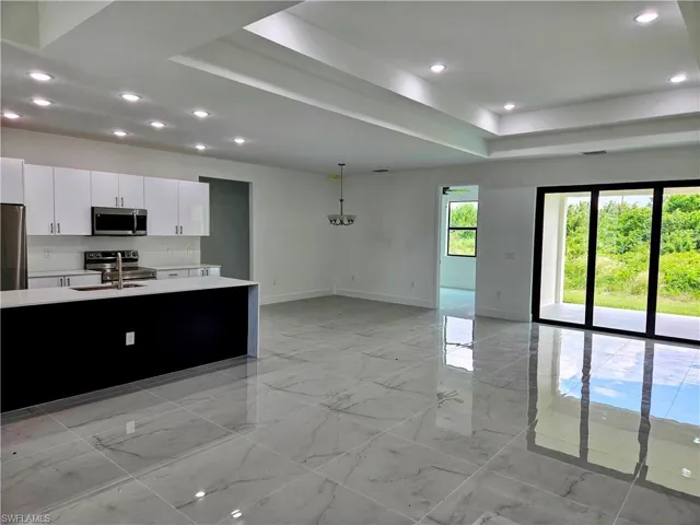 Kitchen featuring stainless steel appliances, decorative light fixtures, a raised ceiling, white cabinets, and light tile patterned floors