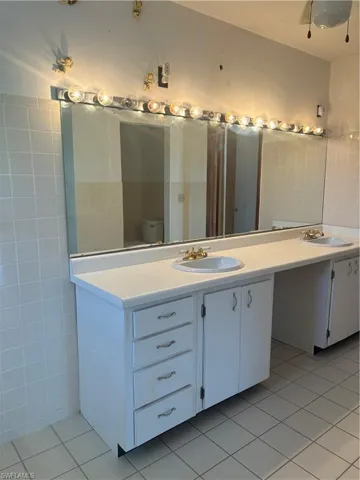 Bathroom featuring dual bowl vanity, tile walls, tile patterned floors, and toilet