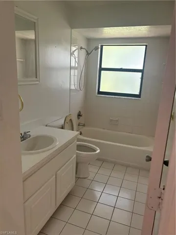 Full bathroom with vanity, tiled shower / bath combo, toilet, and tile patterned flooring