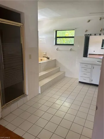 Bathroom featuring tile patterned floors, tile walls, vanity, and tiled bath