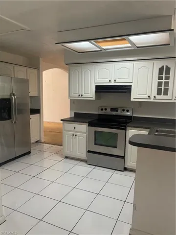 Kitchen with light tile patterned floors, extractor fan, stainless steel range with electric cooktop, and white refrigerator