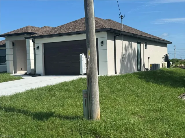 View of side of home featuring a garage, a lawn, and central AC unit