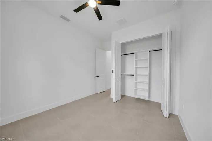 Light-toned tile flooring, ceiling fan with light fixture, bifold closet doors, built-in closet shelving, and a panel door with dark hardware
