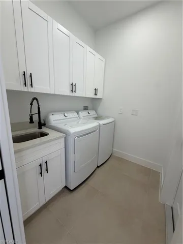 Laundry room featuring white cabinetry, a utility sink with a matte black faucet, and large format floor tiling