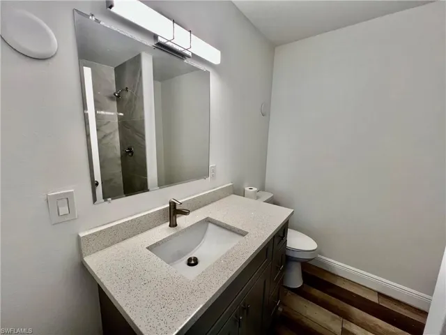 Full bathroom with toilet, a tile shower, baseboards, wood finished floors, and vanity