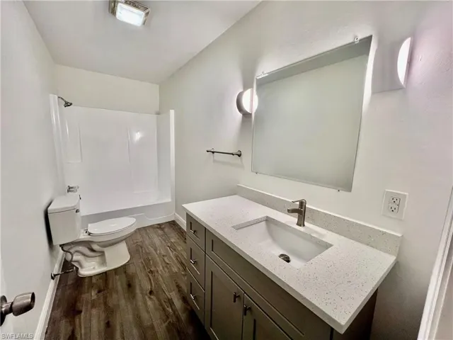 Bathroom featuring washtub / shower combination, wood finished floors, toilet, and vanity