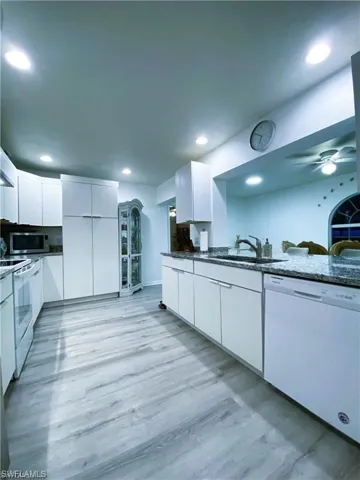 Kitchen with white cabinetry, modern cabinets, dark stone countertops, white appliances, and light wood-style floors