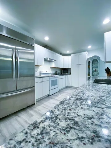 Kitchen with stainless steel appliances, white cabinetry, light stone countertops, light wood finished floors, and recessed lighting