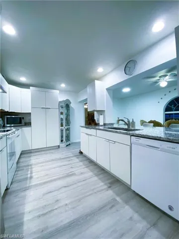 Kitchen with white cabinets, modern cabinets, dark stone countertops, white appliances, and light wood-style flooring