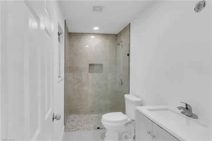 Bathroom featuring toilet, vanity, and tiled shower