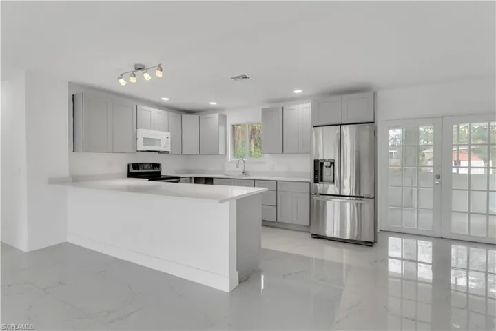 Kitchen with kitchen peninsula, stainless steel refrigerator with ice dispenser, a healthy amount of sunlight, and black / electric stove