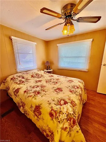 Bedroom featuring wood finished floors, ceiling fan, wood walls, and a textured ceiling