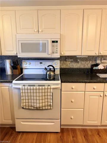 Kitchen with white appliances, white cabinets, and backsplash