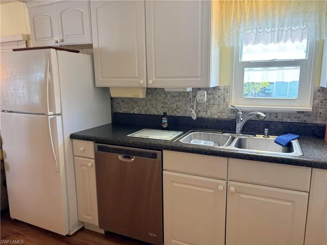 Kitchen with dark countertops, dishwasher, white cabinetry, freestanding refrigerator, and dark wood-style floors