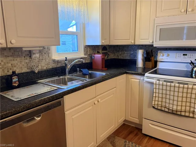 Kitchen featuring white appliances, dark countertops, and white cabinets