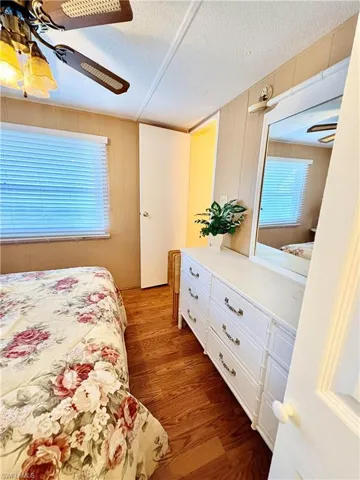 Bedroom featuring dark wood finished floors, a textured ceiling, a ceiling fan, and wooden walls