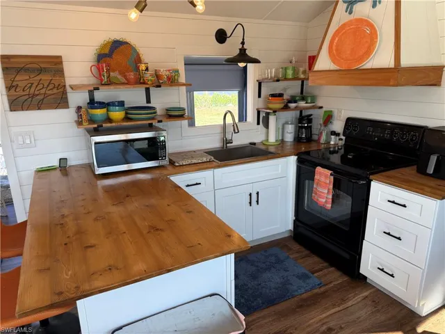 Kitchen with butcher block counters, black range with electric cooktop, white cabinetry, extractor fan, and stainless steel microwave