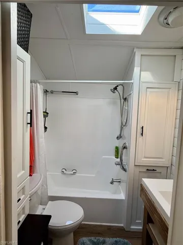 Bathroom with vanity, shower / bathtub combination with curtain, a skylight, and dark wood-style flooring