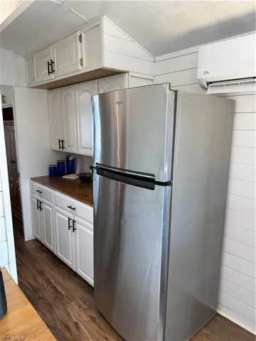 Kitchen with freestanding refrigerator, white cabinets, dark wood-type flooring, and wooden counters